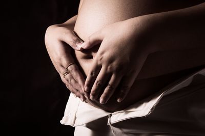 Midsection of woman touching finger against black background