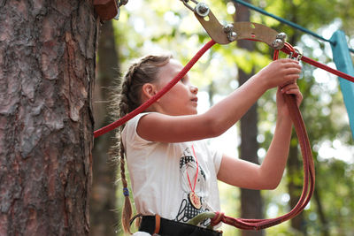 Low angle view of girl attaching safety harness on rope in forest