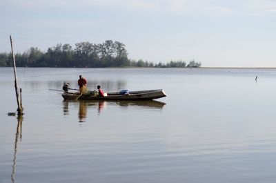 People on boat in lake against sky