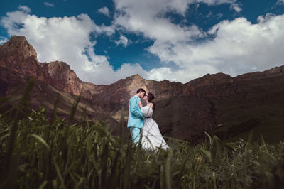 A young man and his wife stand in an embrace high in the mountains against the backdrop of epic