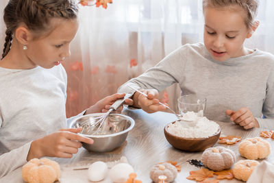 Two cute girls whip gingerbread dough to make halloween cookies in home kitchen. 