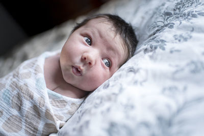 Cute baby girl wrapped in blanket looking away while lying on bed