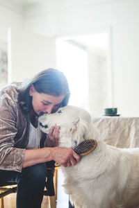 Loving senior woman combing cute dog while sitting at home