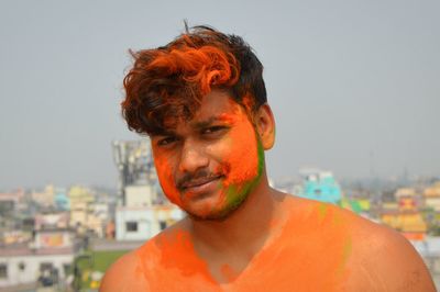 Portrait of shirtless man with orange powder paint on face against sky