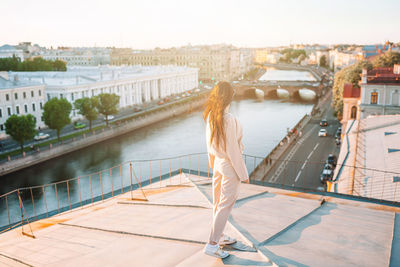 Rear view of woman standing on bridge over river in city