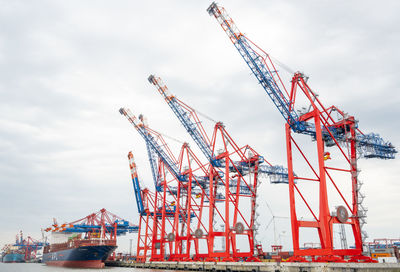 Cranes at commercial dock against sky