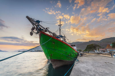 Fishing boat moored in sea against sky during sunset