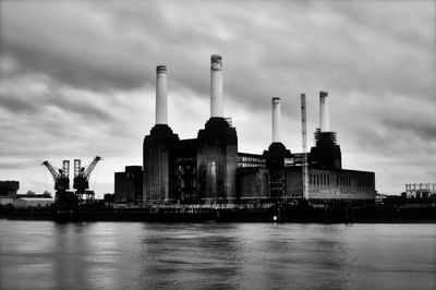 Factory by river against sky in city