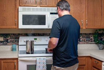 Rear view of man cooking food on stove at home