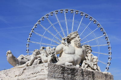 Low angle view of sculpture against ferris wheel and sky