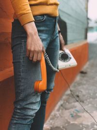 Midsection of man holding umbrella standing against orange city