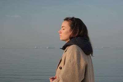 Side view of young woman standing against sea