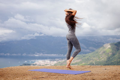 Full length of woman exercising on cliff against sky