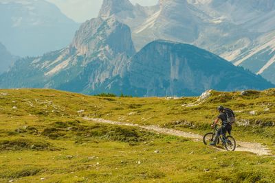 Hiker riding bicycle on field against rocky mountains