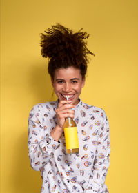 Portrait of smiling young woman holding drink against yellow background