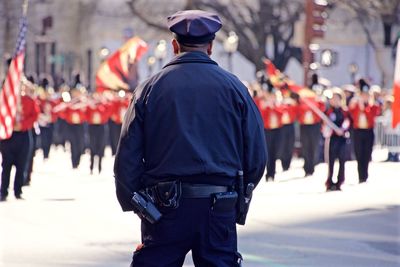 Rear view of police officer standing on road looking at st patricks day parade