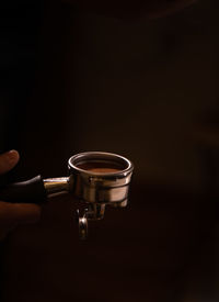 Close-up of hand holding tea cup against black background