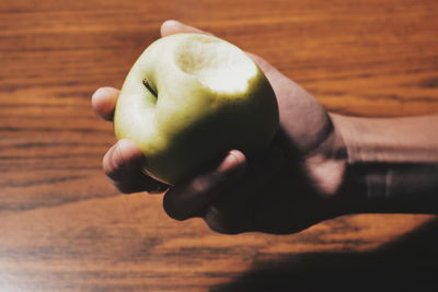 Cropped hand holding apple at wooden table