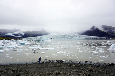 High angle view of person standing against glacier in lake