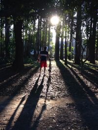 Rear view of person with bike and sun shining through trees in forest