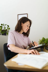 Side view of woman drawing picture on graphic tablet while sitting at table in home office