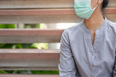 Midsection of woman wearing mask sitting on bench