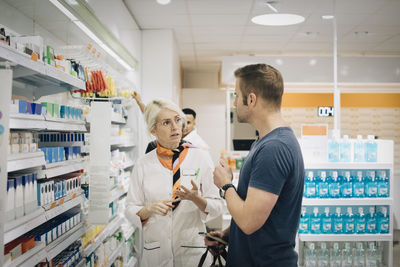 Male customer talking with female owner standing by rack at pharmacy store