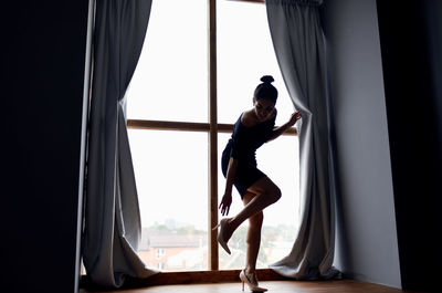 Side view of woman standing by window at home