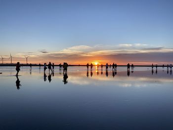 Silhouette people on wooden post by sea against sky during sunset