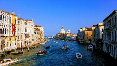 Boats in canal amidst buildings against clear sky