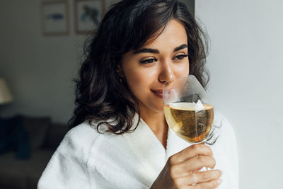 Close-up of smiling woman drinking wine while standing at home