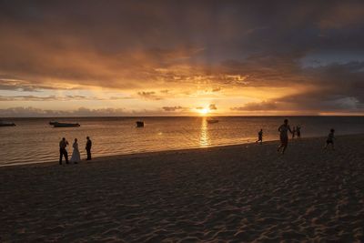 Silhouette people on beach against sky during sunset