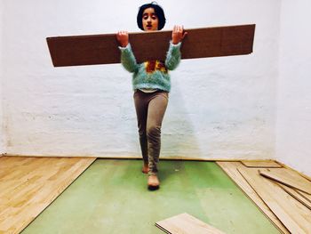 Girl holding wood while walking against wall