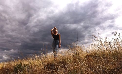 Low angle view of woman standing on field against cloudy sky