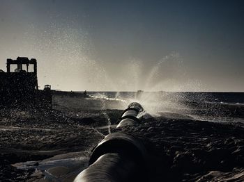 Close-up of pipe splashing water against sky