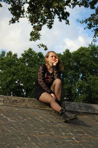 Happy young woman sitting against trees and plants