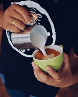 Midsection of woman pouring latte in coffee cup