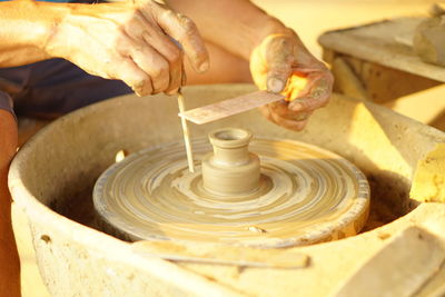 Cropped hands of potter by pottery wheel