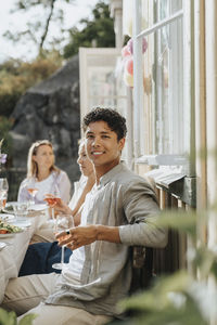 Portrait of smiling young man holding wineglass during dinner party at cafe