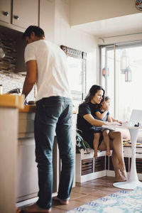 Mother and daughter using laptop while father working in domestic kitchen