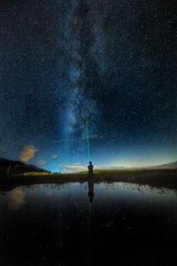Silhouette person with flashlight standing by lake against star field at night