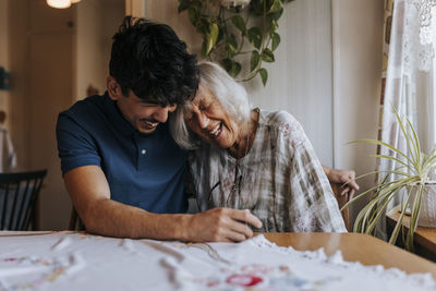 Happy senior woman leaning on male caregiver's shoulder at home