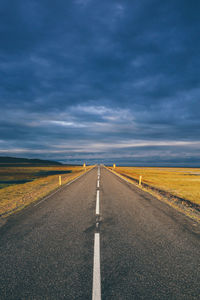 Empty road amidst field against cloudy sky