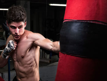 Shirtless man punching bag in boxing rink