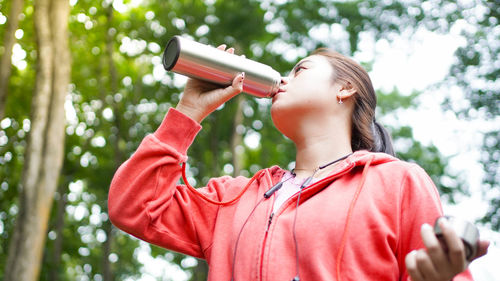 Low angle view of woman holding plant against trees