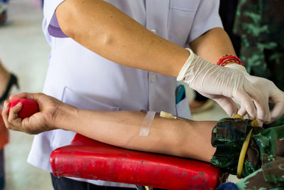 Midsection of nurse tying rubber band on patient hand at blood donation camp