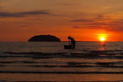 Silhouette man in sea against orange sky