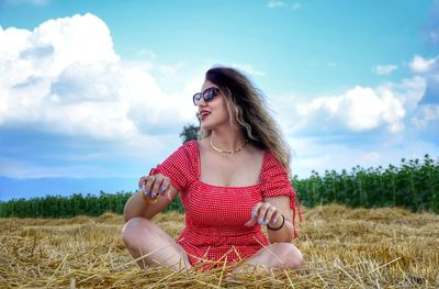 Young woman wearing sunglasses while sitting on field against sky