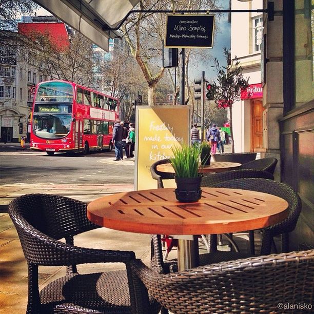 chair, text, table, communication, western script, empty, absence, architecture, seat, restaurant, built structure, cafe, building exterior, day, sidewalk cafe, non-western script, potted plant, sunlight, no people, bench