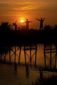 Silhouette people standing by lake against sky during sunset